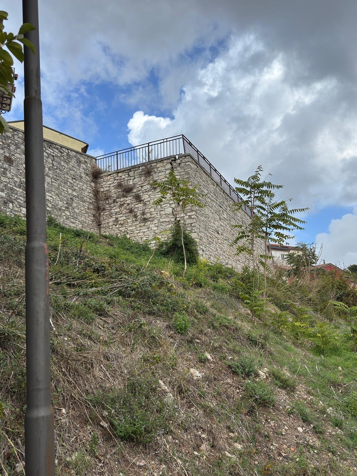Muro di sostegno in pietra a monte del muro crollato, con una lesione verticale nell'angolo sotto la ringhiera
