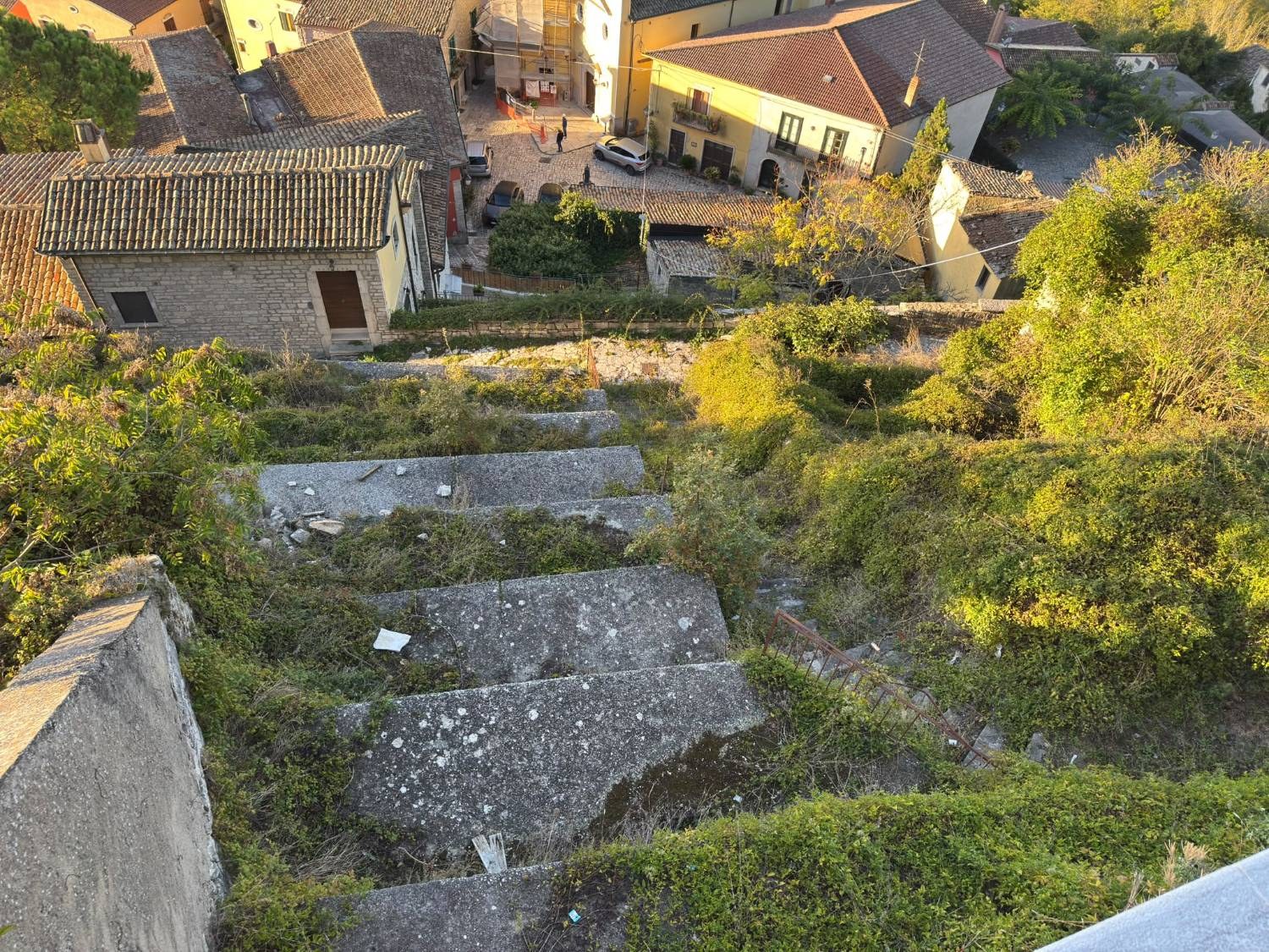 La scalinata a valle della Chiesa Madre vista dal belvedere, con i gradoni coperti dalla vegetazione e la ringhiera arrugginita